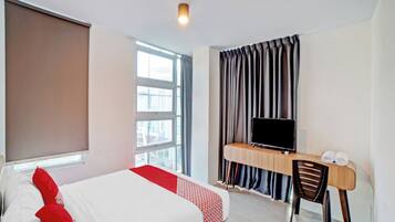 A hotel room with a bed, a desk with a chair, a television, and a window with curtains.