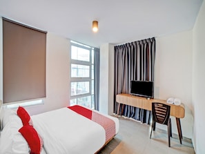 A hotel room with a bed, a desk with a chair, a television, and a window with curtains. - OYO 90559 Gamacity Residence (Medan)
