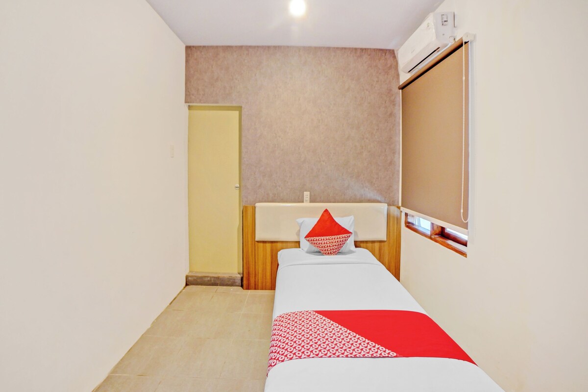 Una stanza piccola e pulita con un letto singolo, un comodino, uno specchio e una finestra.