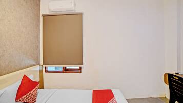 A hotel room with a bed, a window with a blind, a desk, and a chair.