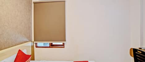 A hotel room with a bed, a window with a blind, a desk, and a chair.
