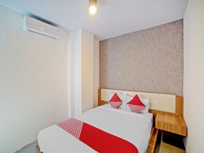 Camera d'albergo con un letto, un comodino in legno, una coperta con motivo rosso e bianco e una parete beige con texture.