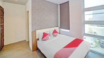 A modern hotel room with a large bed, a window with a view of the city, and a door to the left.