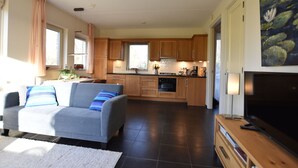 A modern living room with a grey sofa, wooden cabinets, and a flat-screen TV. - Rural holiday home with terrace (Zuidwolde)