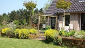 A house with a brick exterior, a tiled roof, and a garden with yellow flowers and a wooden pergola. - Rural holiday home with terrace (Zuidwolde)