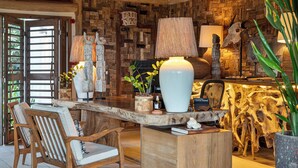 Un coin bar en bois au design rustique, agrémenté d’une grande sculpture en bois, d’un vase blanc et d’une plante en pot.