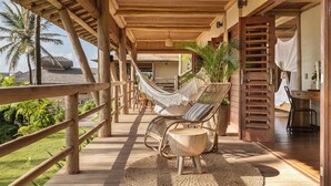 Une terrasse en bois avec un hamac, des fauteuils en osier et une table en bois.