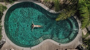 Vue aérienne d’une piscine à bord incurvé, entourée d’une terrasse en bois et de murs en pierre.
