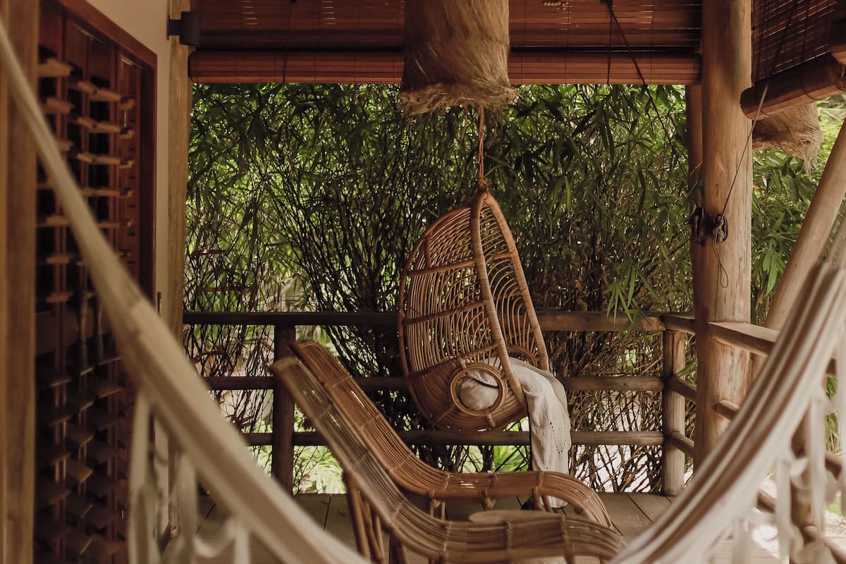Una silla hamaca en una terraza de madera con vista a árboles de bambú.