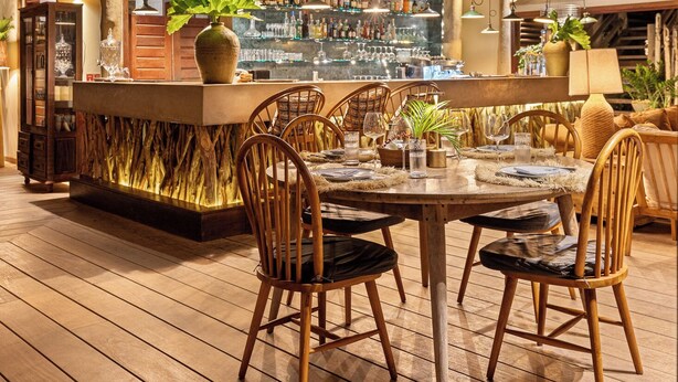Une terrasse en bois avec un coin bar, des chaises en bois et des plantes suspendues.