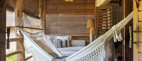 A hammock bed in a wooden room with a thatched roof and a hanging light fixture.