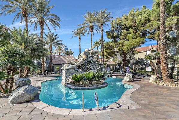 Relax by the serene pool surrounded by lush greenery and a natural stone pathway.