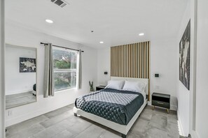 Relax in a serene space with a large bed, a bedside table, and a window offering a view of lush greenery.