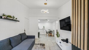 Ein modernes Wohnzimmer mit einem grauen Sofa, einem Flachbildfernseher, der an einer Holzplatte angebracht ist, und einem kleinen Kaktus auf der Kommode.