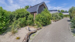 A modern house with a unique curved roof, surrounded by dense greenery and a gravel driveway.