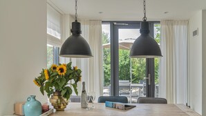 A dining area with a wooden table, four chairs, a vase of sunflowers, a bottle of champagne, and two pendant lights.