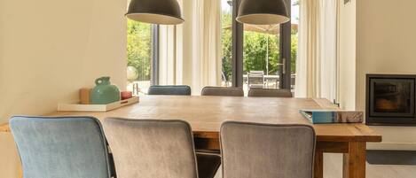 Comedor con mesa de madera, cuatro sillas, dos lámparas colgantes y vista a zonas verdes al exterior.