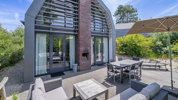 A modern house with a large glass door, outdoor seating area, and a patio with a table and chairs.