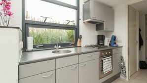 Une cuisine moderne dotée d’une fenêtre, d’appareils électroménagers en acier inoxydable et offrant une vue sur la verdure environnante.