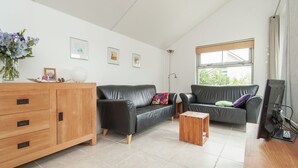Un salon moderne avec un meuble en bois, deux canapés en cuir noir, une petite table basse en bois et une grande fenêtre donnant sur un paysage verdoyant.