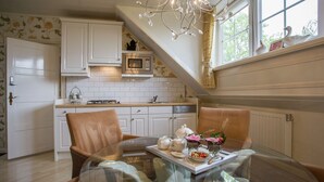 A kitchen with white cabinets, a microwave, and a dining area with a glass table and chairs. - Boutique Apartment in Ritthem with Terrace (Vlissingen-Ritthem)