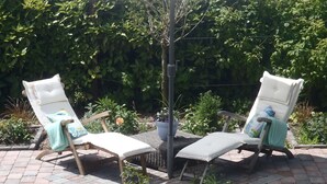 Two lounge chairs with white cushions and blue towels, a white umbrella, and a potted plant in a garden setting. - Boutique Apartment in Ritthem with Terrace (Vlissingen-Ritthem)