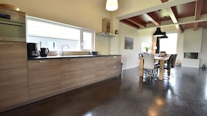 Een ruime keuken met houten kastjes, een groot raam en een eethoek met een tafel en stoelen.