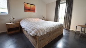 Een slaapkamer met een houten bed, twee nachtkastjes met lampen, een raam met gordijnen en een schilderij aan de muur.