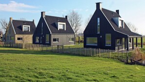 Een rij moderne huizen met steile daken en grote ramen, omgeven door een houten hek en een gazon.