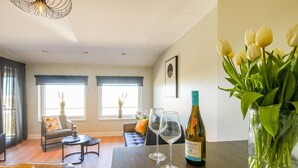 Un salon moderne avec une table en bois, deux chaises, un canapé et un vase de tulipes. On peut voir deux verres à vin et une bouteille de vin sur la table.