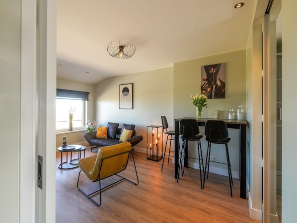 A modern living room with a sofa, chairs, a dining area, and a kitchen counter.