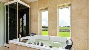 Un bagno moderno con una grande vasca, un box doccia in vetro e vista su un campo verde dalle finestre.