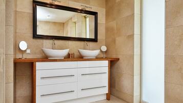 A bathroom with a wooden vanity, two white vessel sinks, a large mirror, and a window.