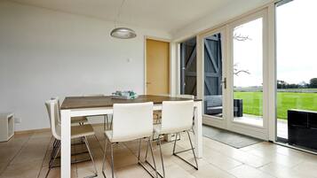 A dining area with a wooden table and white chairs, a pendant light, and a view through a glass door to an outdoor area.