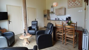 Una sala de estar moderna con sofás de cuero negro, una mesa de comedor de madera con cuatro sillas, una pequeña mesa de centro de madera y una zona de cocina con armarios de madera y un microondas.