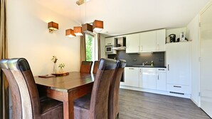 A modern kitchen with white cabinets, a wooden dining table, and leather chairs. - Chalet in Reutum with Sauna and Nature (Reutum-Weerselo)