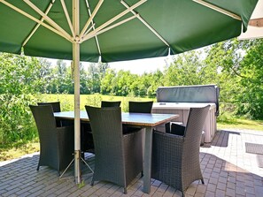 An outdoor patio with a table and chairs, a grill, and a green umbrella. - Chalet in Reutum with Sauna and Nature (Reutum-Weerselo)