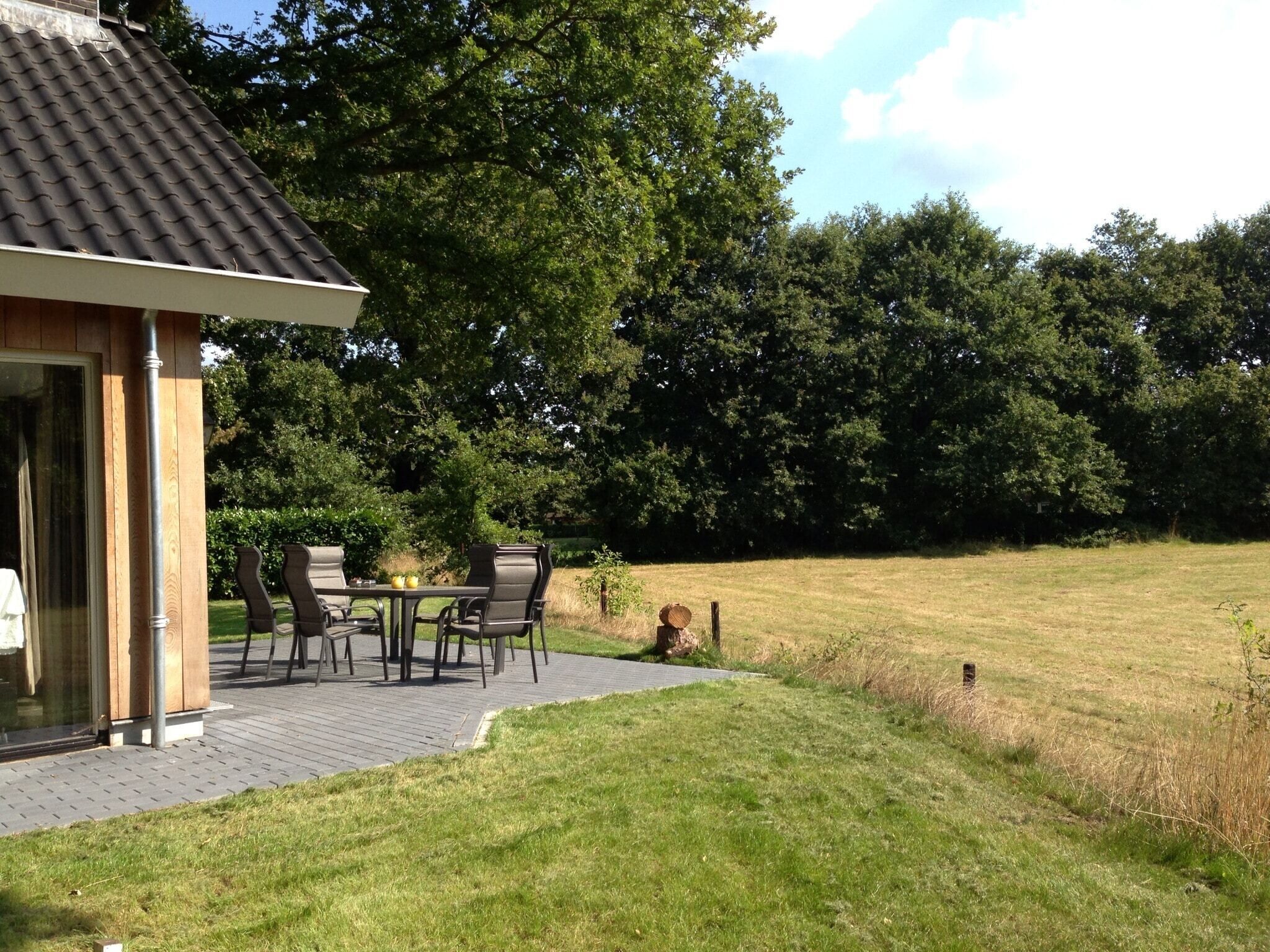 A patio with a table and chairs, a fire pit, and a view of a grassy field and trees.