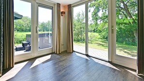 A room with large sliding glass doors leading to a garden. - Chalet in Reutum with Sauna and Nature (Reutum-Weerselo)