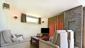 A modern living room with a flat-screen TV, two sofas, a coffee table, and a stone accent wall. - Chalet in Reutum with Sauna and Nature (Reutum-Weerselo)