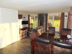 A spacious living room with a large wooden dining table, leather chairs, and a built-in fireplace. - Chalet in Reutum with Sauna and Nature (Reutum-Weerselo)