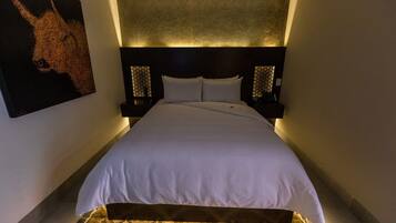 A hotel room with a large bed, a headboard with a textured design, two bedside tables with lamps, and a patterned rug on the floor.