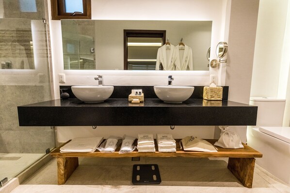 Une salle de bain moderne avec deux lavabos, un grand miroir et une étagère en bois où sont posées des serviettes.