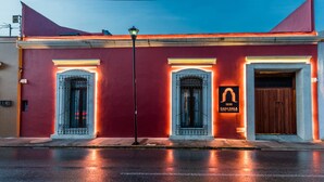 A building with a red facade, two arched windows with metal grilles, a wooden door, and a sign reading "CASA NAILA HOTEL BOUTIQUE". - Casa Naila Hotel Boutique (Oaxaca)