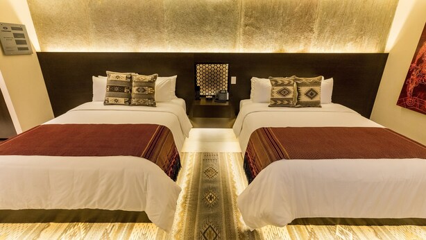 A hotel room with two beds, a patterned rug, and a headboard with built-in lighting. - Casa Naila Hotel Boutique (Oaxaca)