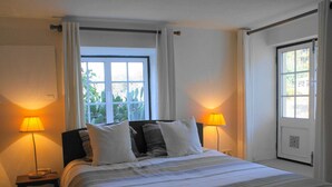 A bedroom with a bed, two bedside lamps, a window, and a door. - Idyllic Country Cottage with Forest (Covas)