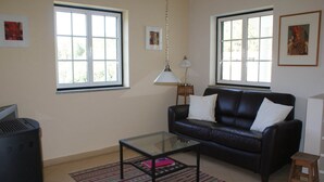 A living room with a black leather sofa, a glass coffee table, a patterned rug, and two windows with white frames. - Idyllic Country Cottage with Forest (Covas)