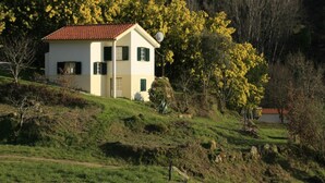 A two-story house with a red-tiled roof, situated on a grassy hill with trees in the background. - Idyllic Country Cottage with Forest (Covas)