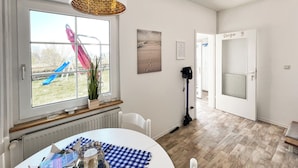 Een kamer met een eettafel, een raam met uitzicht op een speeltuin, een radiator en een deur met de tekst 'Diego 9'.