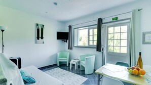 Habitación de hotel con cama, escritorio con frutero, dos sillas, televisión y ventana con cortinas.